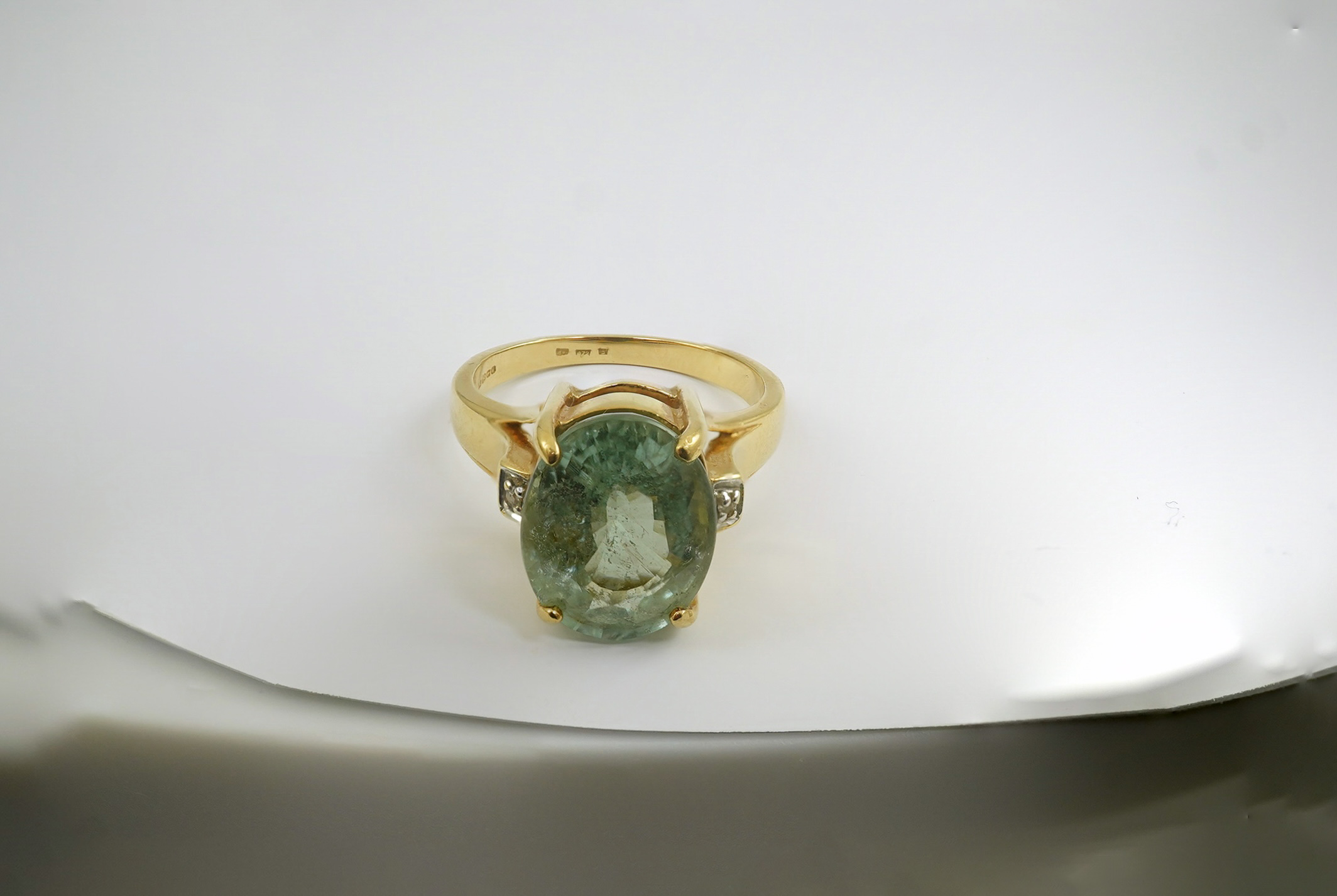 A modern 18ct gold and oval cut pale green tourmaline set dress ring, with two stone diamond chip set shoulders